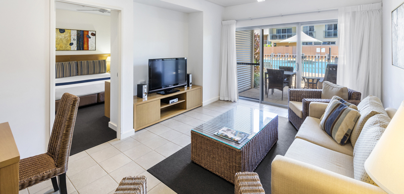 plasma TV with Foxtel in front of comfortable couch in air conditioned living room of 1 bedroom apartment with private balcony at Oaks Broome hotel in Western Australia